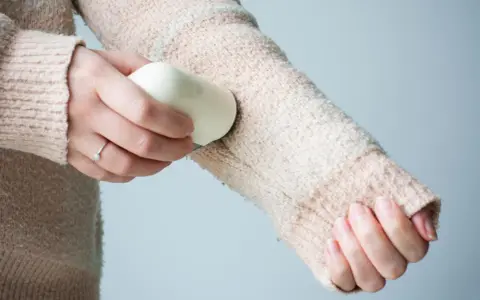 Frauenhand entfernt mit einem Hausmittel Fussel von einem Strickpullover.