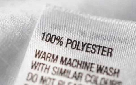 Etikett zeigt "100% POLYESTER". Pflegehinweise für das pflegeleichte Polyester-Material.