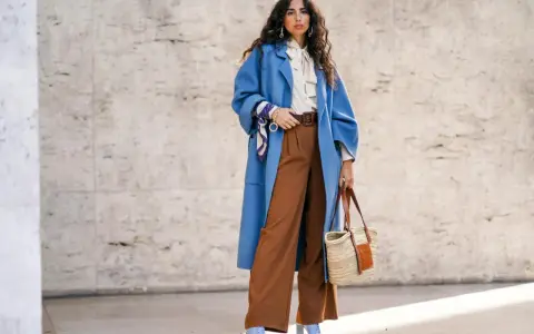 Stilvolles Outfit: Blaue Oversize-Jacke, cremefarbene Bluse mit Schleife und braune weite Hose kombinieren. Accessoires: Korbtasche, Gürtel, Halstuch.