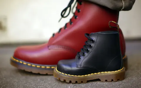 Ein roter und ein schwarzer Dr. Martens Stiefel, die die lange **Dr. Martens Geschichte** von robusten Schuhen für alle Generationen symbolisieren.