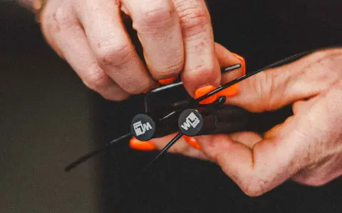 Hände mit orangen Nägeln stellen ein Springseil ein. Die Griffe haben ein Logo.