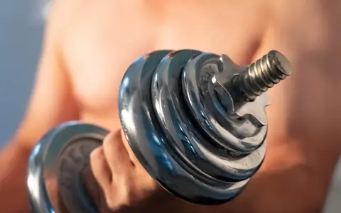 Mann hebt Hantel. Die Frage "wie lange dauert muskelaufbau" beschäftigt viele Fitnessbegeisterte.