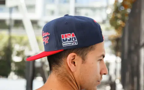 Junger Mann trägt eine dunkelblaue Kappe mit rotem Schirm und "USA Basketball"-Aufdruck, den **cap nach hinten tragen** ist sein Stil.