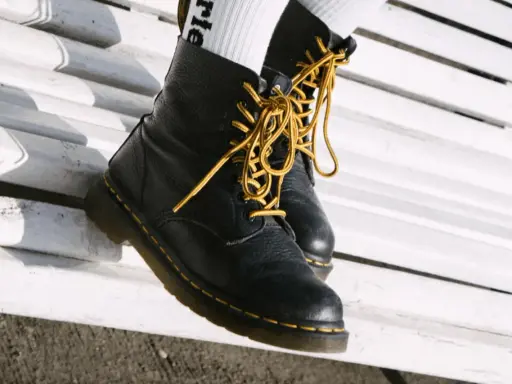 Schwarze Dr. Martens mit gelben Schnürsenkeln auf einer weißen Bank. Sie fallen eher groß aus, also lieber eine Nummer kleiner wählen.