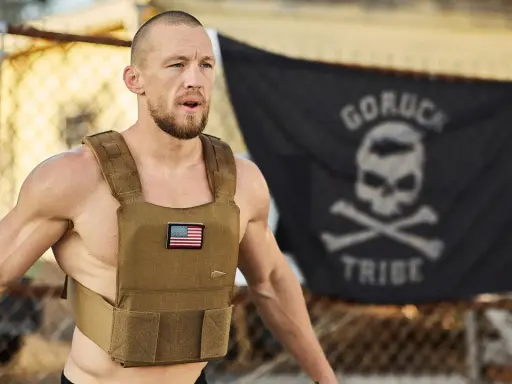 Mann mit Gewichtsweste und GORUCK-Flagge im Hintergrund, bereit für die Murph Challenge.