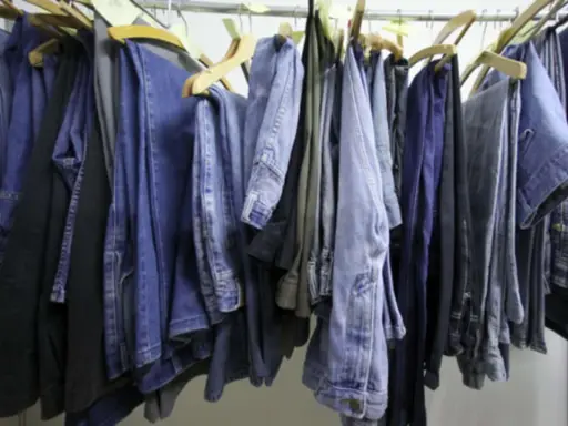 Eine Reihe von Jeans hängt an Kleiderbügeln. Manche sind hellblau, andere dunkelblau. Sie sind bereit, um sie bei 60 Grad zu waschen.