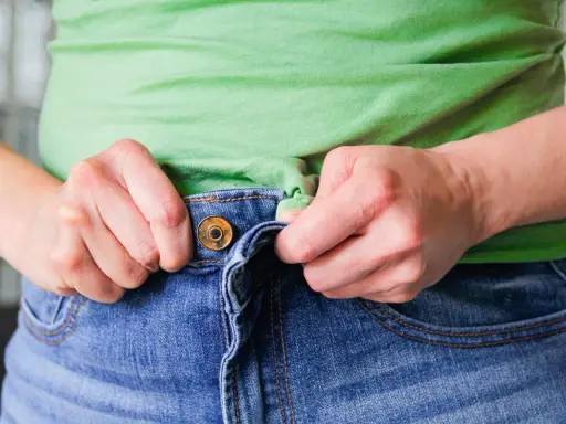 Hände ziehen am Bund einer Jeans, um sie weiter zu machen.