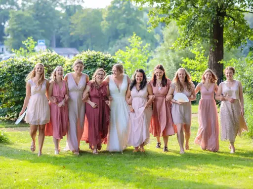 Brautjungfern in zarten Rosatönen, ein perfekter **dresscode hochzeit**, spazieren lachend über eine grüne Wiese.