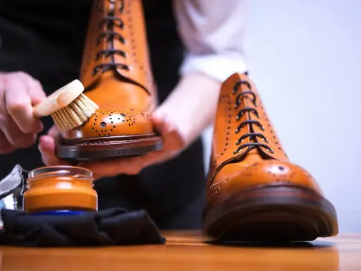Hände bürsten braune Lederschuhe, um sie zu reinigen. Daneben steht eine Dose Schuhcreme.