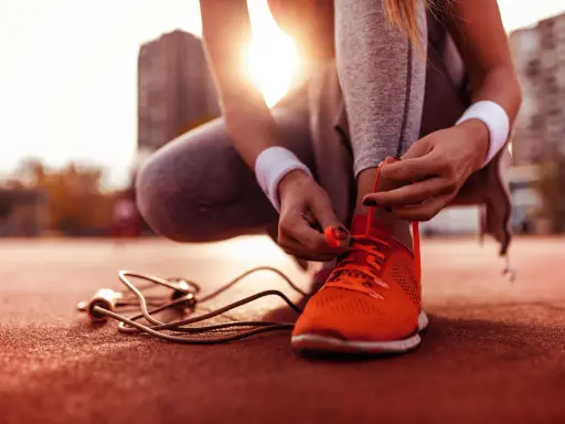Sportlerin bindet ihre neuen, leuchtend orangen Laufschuhe ein. Die Sonne scheint, ein Springseil liegt bereit.
