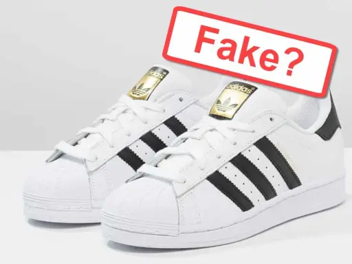 Zwei weiße Adidas Superstar Sneaker mit schwarzen Streifen. Ein rotes Schild fragt: "Fake?". So kannst du Adidas fake erkennen.
