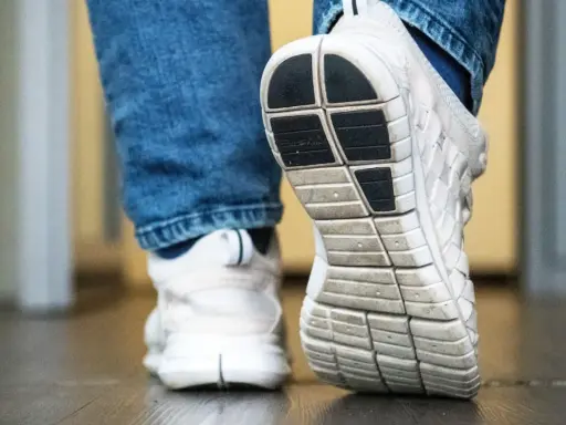 Weiße Turnschuhe mit Jeans. Die Sohle der Schuhe quietschen auf dem Boden, als jemand einen Schritt macht.