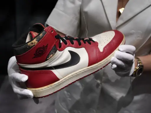 Ein Paar rote und weiße Air Jordan 1 Sneaker, die als die teuersten Schuhe der Welt gelten, werden von Händen in weißen Handschuhen gehalten.