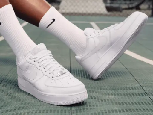 Weiße Nike Air Force 1 Sneaker mit schwarzen Socken auf einem grünen Untergrund. Perfekt zum Air Force 1 binden und loslegen.