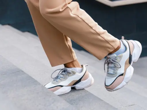 Schritte aufwärts in beigen Hosen und trendigen Sneakern mit sichtbaren Socken. Der socken in sneaker trend ist hier perfekt umgesetzt.