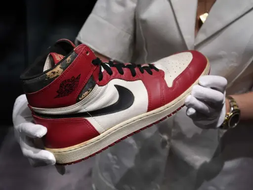 Ein ikonischer Air Jordan 1 Sneaker, der die Nike Air Jordan Geschichte verkörpert, wird von Händen in weißen Handschuhen präsentiert.