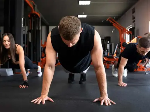 Drei Personen machen Liegestütze im Fitnessstudio. Sie lernen, was sind Burpees, eine Ganzkörperübung.