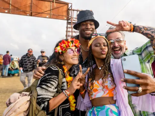 Bunte Outfits, Blumenkränze und Peace-Zeichen: So zieht man zu einem Rave an! Vier Freunde machen ein Selfie.