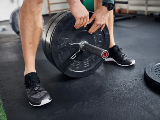 Mann lädt Gewichtsscheiben auf eine Langhantel in einem Fitnessstudio.