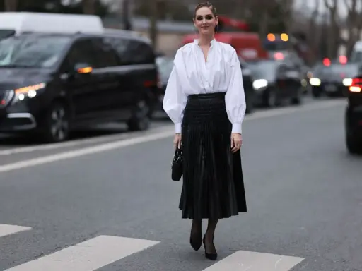 Chic Frau in weißer Bluse und schwarzem oberteil zu plisseerock, steht auf Zebrastreifen.