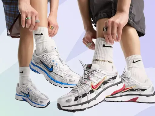 Zwei Paare Nike P-6000 Sneaker in Weiß mit blauen und roten Akzenten. Die Füße tragen weiße Socken mit Nike-Logo und auffälligen Schmuck.