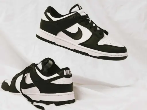 Zwei schwarz-weiße Nike Dunk Low Sneaker schweben auf weißem Stoff. Sie fallen größtenteils größengerecht aus.