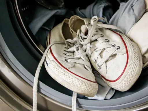 Weiße Turnschuhe mit roten Streifen liegen in einer Waschmaschine, bereit für die Reinigung.