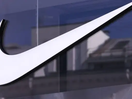 Großes, weißes Nike-Logo auf einer Glasfassade, reflektiert Gebäude im Hintergrund.