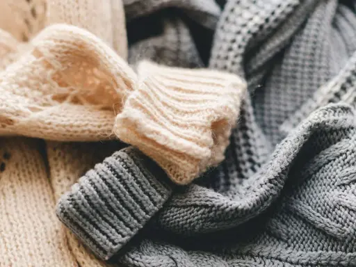 Weiche, gestrickte Pullover in Beige und Grau liegen übereinander. Bald ist Zeit für die **Wolle waschen**, damit sie wieder frisch duften.
