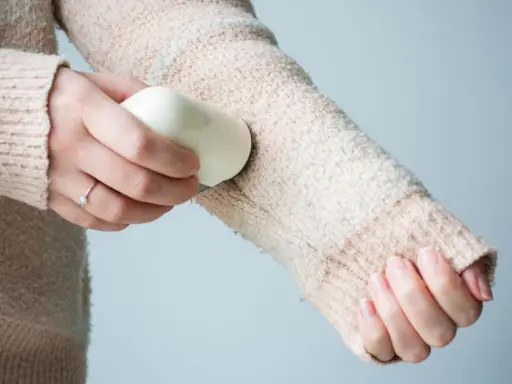 Frauenhand entfernt mit einem Hausmittel Fussel von einem Strickpullover.