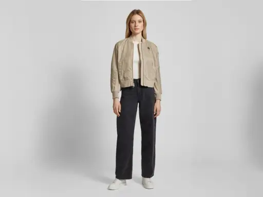 Frau stylt eine beige Bomberjacke mit weiten schwarzen Jeans und weißen Sneakern. Ein lässiger Look, der sich leicht anpassen lässt.