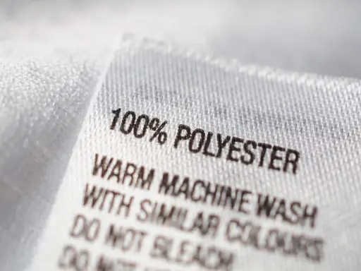 Etikett zeigt "100% POLYESTER". Pflegehinweise für das pflegeleichte Polyester-Material.