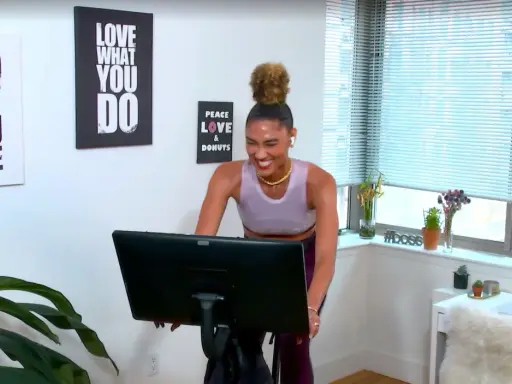 Frau lacht auf einem Heimtrainer, bereit für ein intensives Tabata Workout. Wandbilder motivieren: "Do what you love".