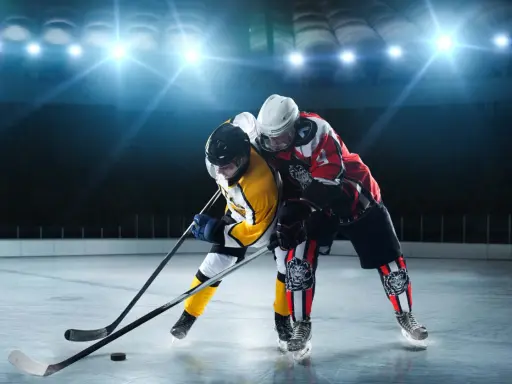 Zwei Eishockeyspieler im Kampf um den Puck. Perfekt, um zu sehen, was anziehen zum Eishockey gucken: warme Kleidung und gute Laune!