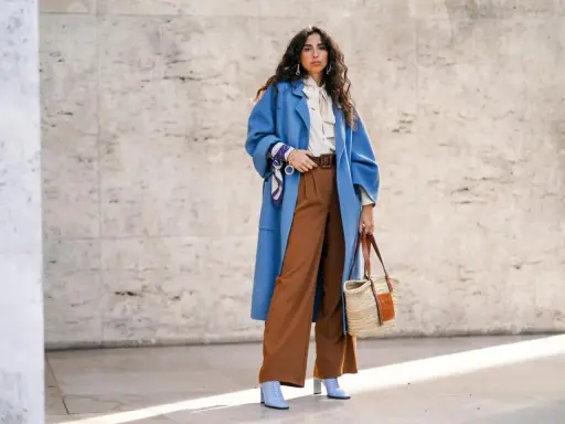 Stilvolles Outfit: Blaue Oversize-Jacke, cremefarbene Bluse mit Schleife und braune weite Hose kombinieren. Accessoires: Korbtasche, Gürtel, Halstuch.