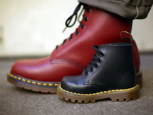 Ein roter und ein schwarzer Dr. Martens Stiefel, die die lange **Dr. Martens Geschichte** von robusten Schuhen für alle Generationen symbolisieren.