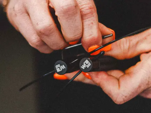 Hände mit orangen Nägeln stellen ein Springseil ein. Die Griffe haben ein Logo.