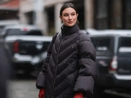 Frau in schwarzer Daunenjacke mit roten Handschuhen im Schnee. Für die Pflege der Daunenjacke im Trockner: welches Programm ist am besten?