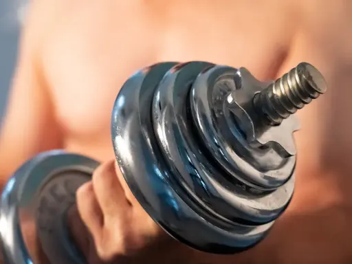 Mann hebt Hantel. Die Frage "wie lange dauert muskelaufbau" beschäftigt viele Fitnessbegeisterte.