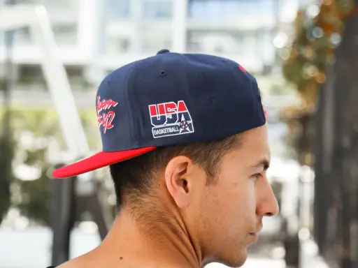 Junger Mann trägt eine dunkelblaue Kappe mit rotem Schirm und "USA Basketball"-Aufdruck, den **cap nach hinten tragen** ist sein Stil.