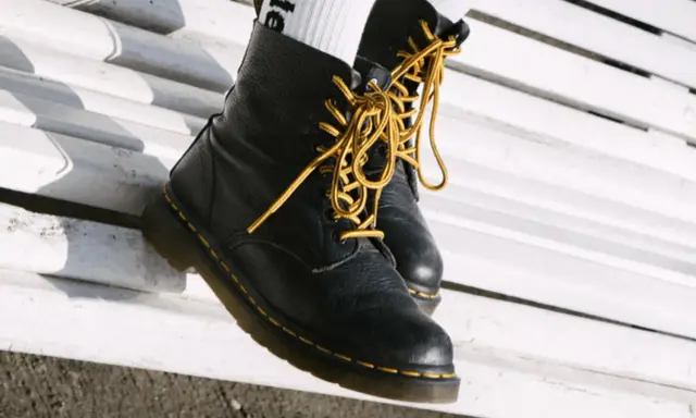 Schwarze Dr. Martens mit gelben Schnürsenkeln auf einer weißen Bank. Sie fallen eher groß aus, also lieber eine Nummer kleiner wählen.