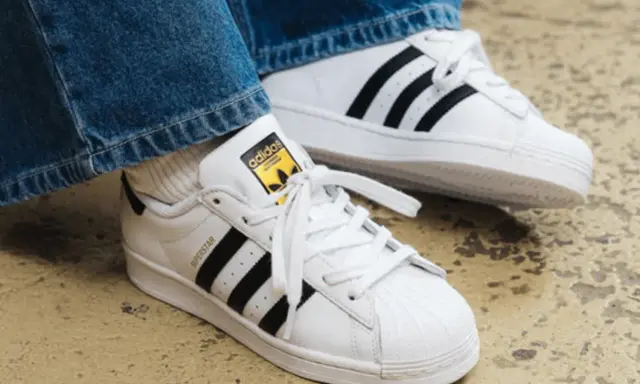 Weiße Adidas Superstar Sneaker mit schwarzen Streifen und gelbem Logo. Perfekt, um das Adidas modell herausfinden.