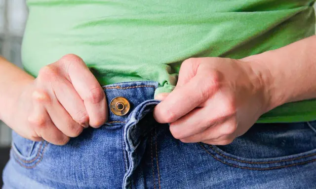 Hände ziehen am Bund einer Jeans, um sie weiter zu machen.