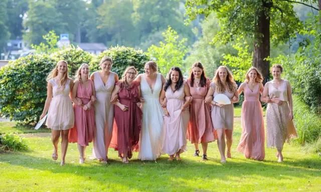 Brautjungfern in zarten Rosatönen, ein perfekter **dresscode hochzeit**, spazieren lachend über eine grüne Wiese.