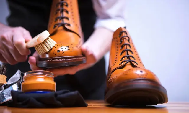Hände bürsten braune Lederschuhe, um sie zu reinigen. Daneben steht eine Dose Schuhcreme.