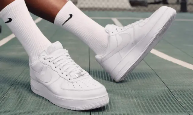 Weiße Nike Air Force 1 Sneaker mit schwarzen Socken auf einem grünen Untergrund. Perfekt zum Air Force 1 binden und loslegen.