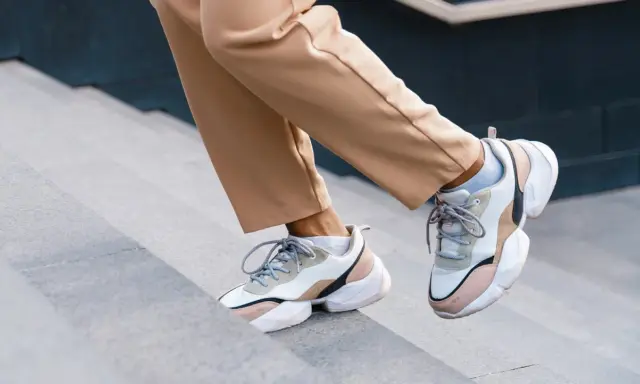Schritte aufwärts in beigen Hosen und trendigen Sneakern mit sichtbaren Socken. Der socken in sneaker trend ist hier perfekt umgesetzt.