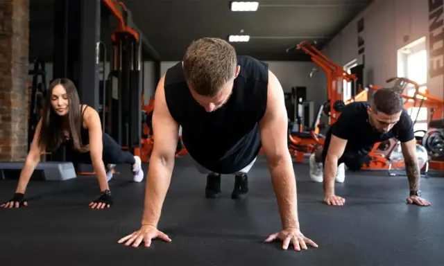 Drei Personen machen Liegestütze im Fitnessstudio. Sie lernen, was sind Burpees, eine Ganzkörperübung.