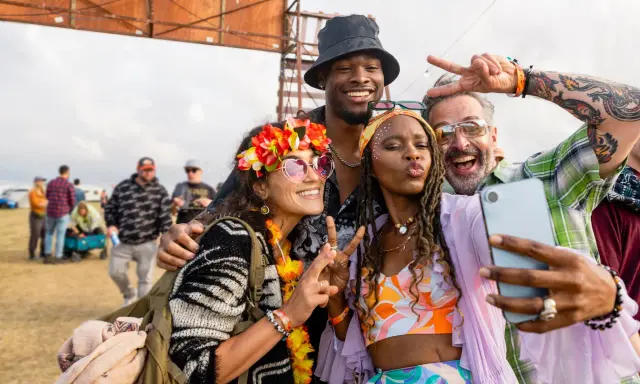 Bunte Outfits, Blumenkränze und Peace-Zeichen: So zieht man zu einem Rave an! Vier Freunde machen ein Selfie.