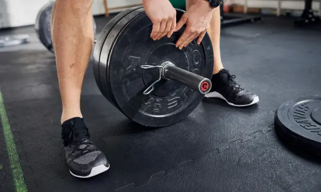 Mann lädt Gewichtsscheiben auf eine Langhantel in einem Fitnessstudio.